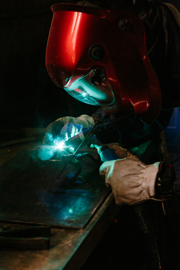 A welder is working on a small piece of bronze. He's melting the metal with a blowtorch. He's wearing protective mask and gloves.
