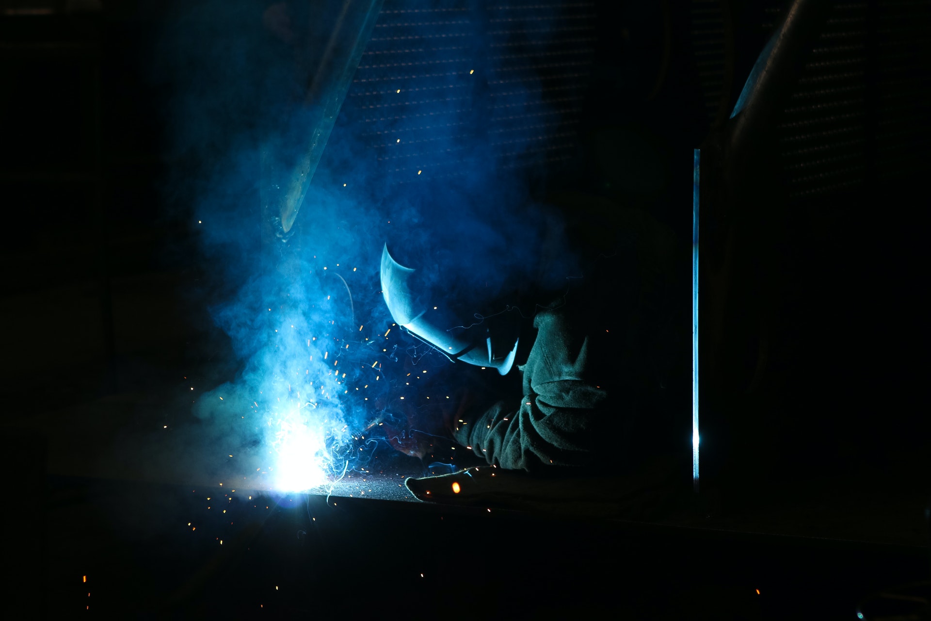 Welder creating blue sparks in a dark workroom.