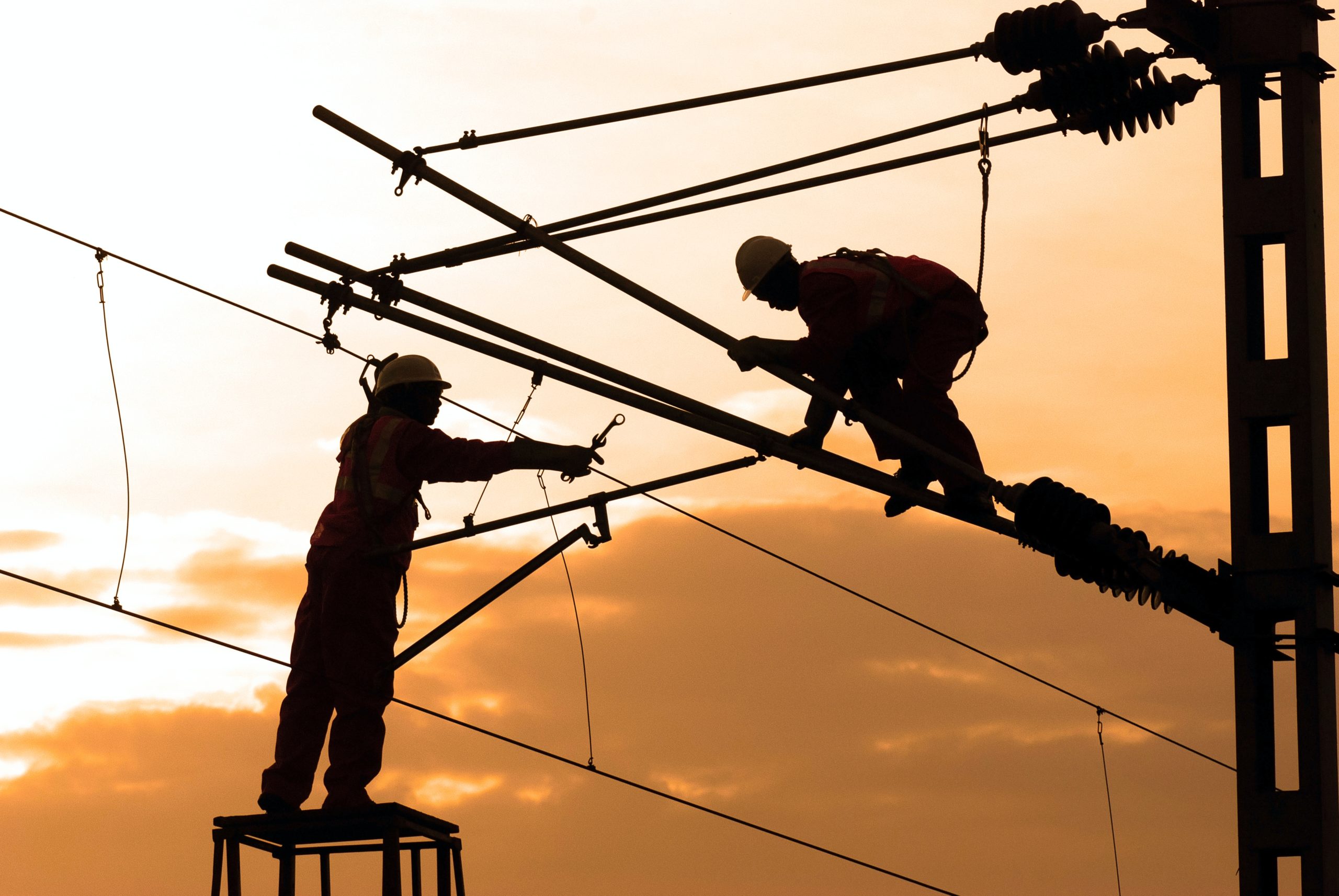 Electrical linemen working at sunset.