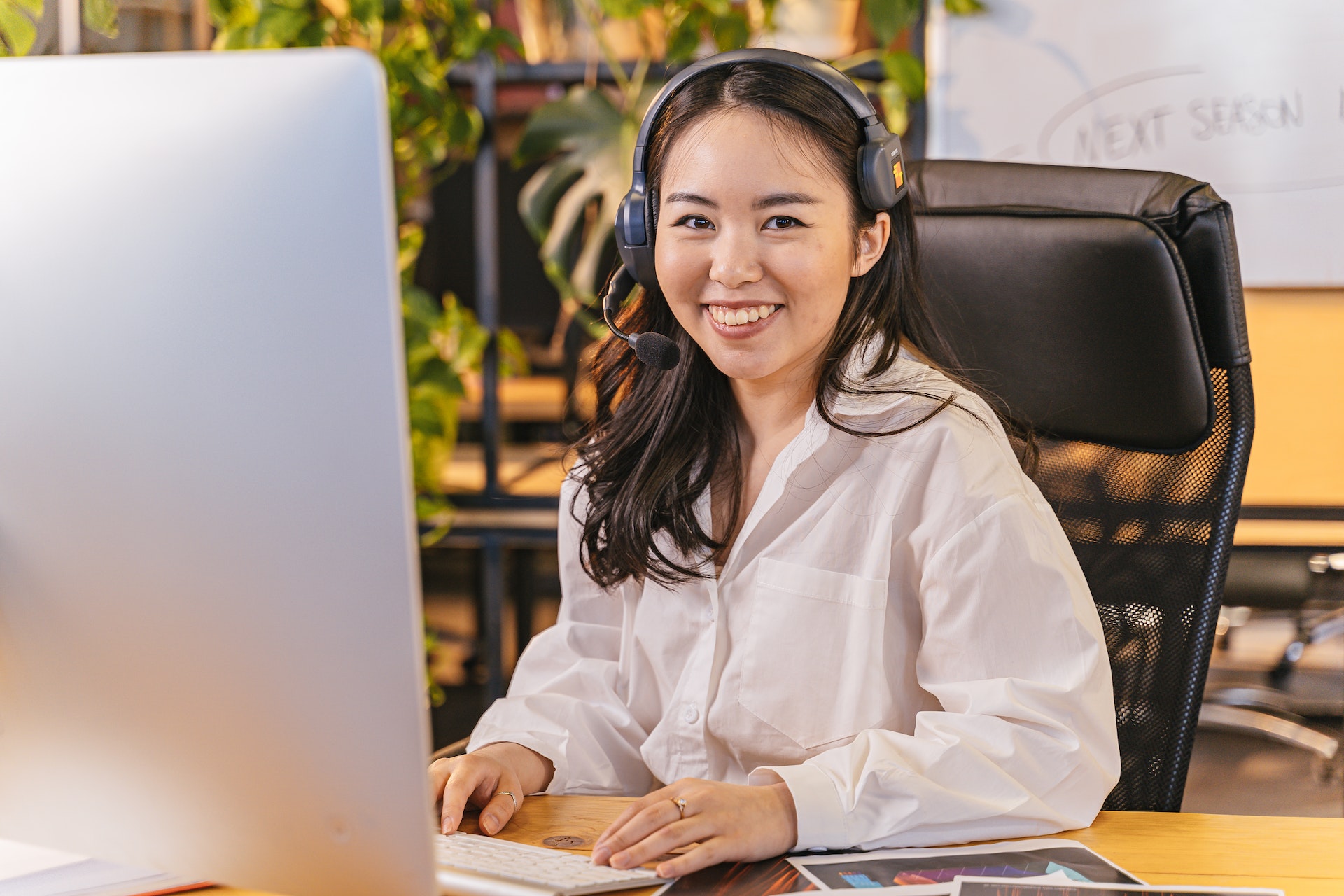 A smiling woman with a headset on sitting at a desk