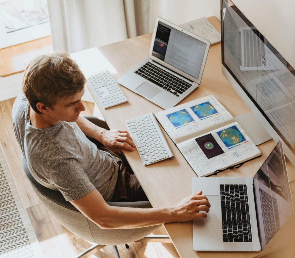 A man working on multiple computers at once with a book open in front of him