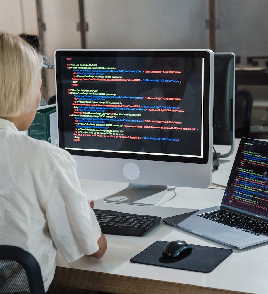 A woman sitting at a desk reading code from two screens