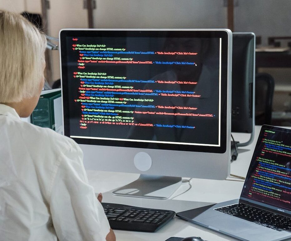 A woman sitting at a desk reading code from two screens